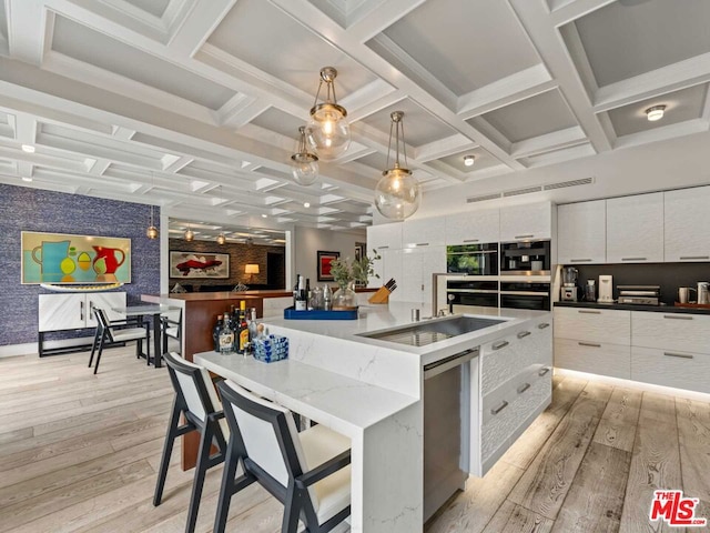 kitchen featuring decorative light fixtures, light wood-type flooring, a large island with sink, stainless steel dishwasher, and white cabinets