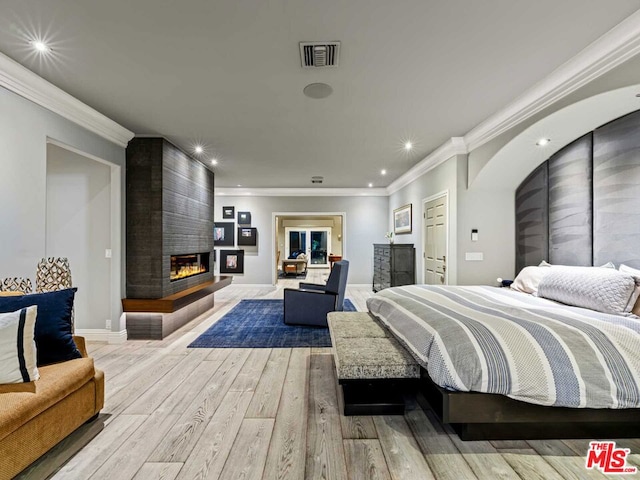 bedroom featuring light wood-type flooring, ornamental molding, and a fireplace