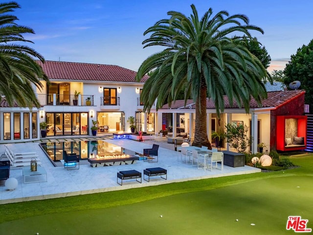 back house at dusk featuring a balcony, a patio, and a fire pit