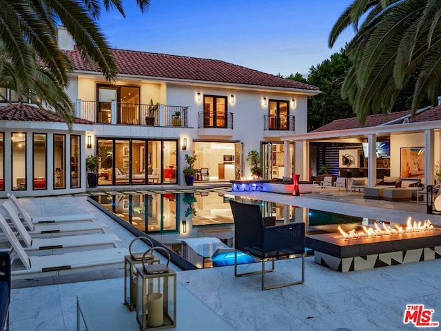 back house at dusk featuring a balcony, a fire pit, and a patio