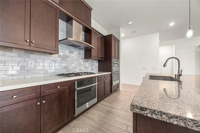 kitchen featuring tasteful backsplash, sink, hanging light fixtures, appliances with stainless steel finishes, and wall chimney exhaust hood