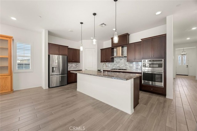 kitchen with stainless steel appliances, wall chimney exhaust hood, tasteful backsplash, and a kitchen island with sink