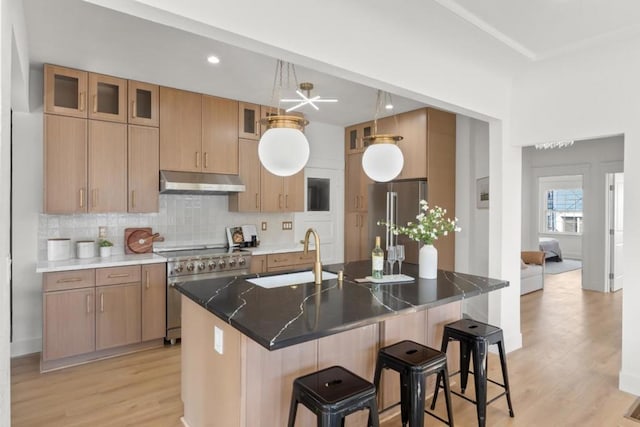 kitchen featuring premium appliances, decorative light fixtures, sink, backsplash, and a center island with sink