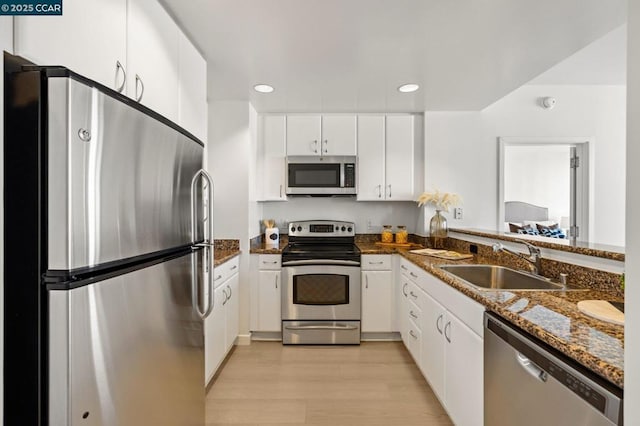 kitchen featuring white cabinetry, light hardwood / wood-style floors, stainless steel appliances, dark stone counters, and sink