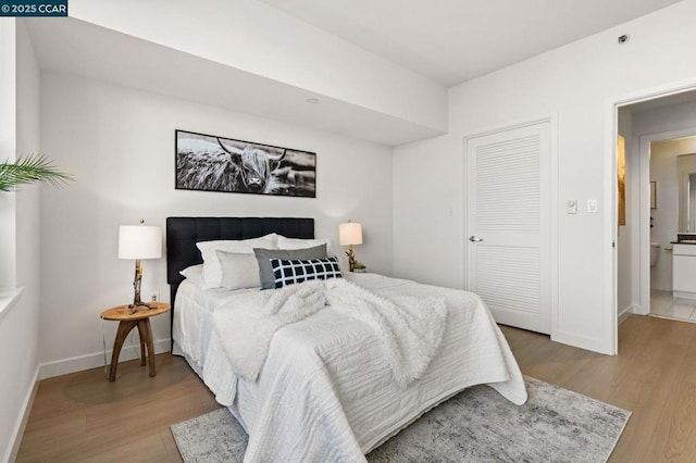 bedroom with ensuite bathroom and light hardwood / wood-style flooring