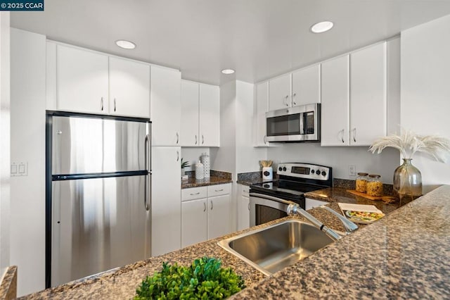 kitchen with appliances with stainless steel finishes, sink, white cabinetry, and dark stone counters