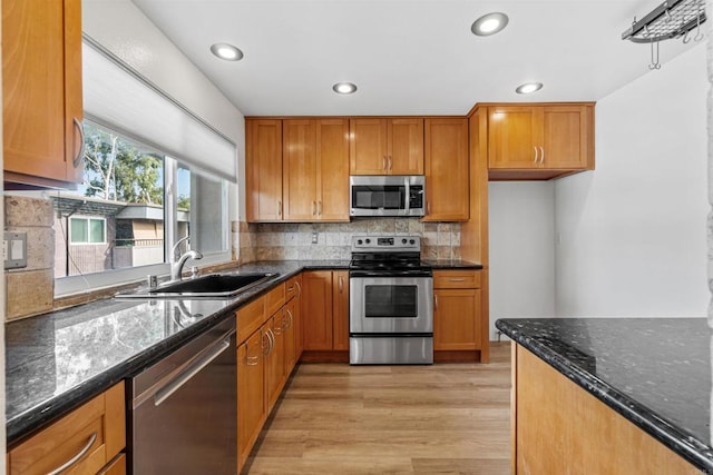 kitchen featuring appliances with stainless steel finishes, dark stone counters, sink, backsplash, and light hardwood / wood-style flooring