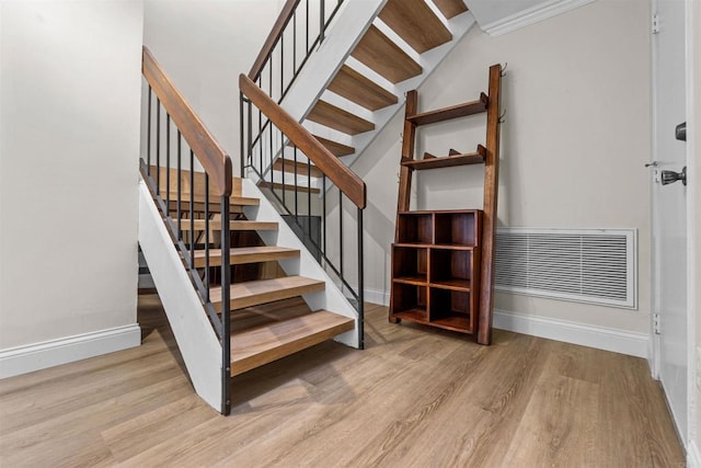 stairway with wood-type flooring and ornamental molding