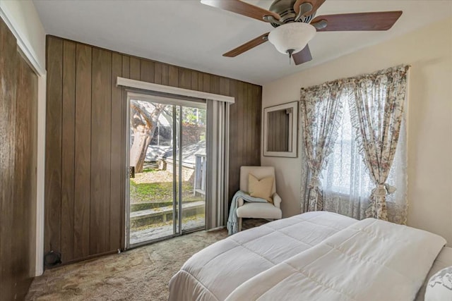 bedroom with a closet, wood walls, access to outside, ceiling fan, and light colored carpet