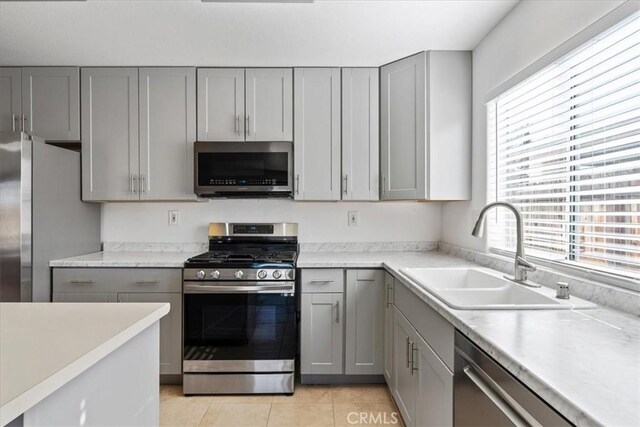 kitchen with light tile patterned floors, appliances with stainless steel finishes, sink, and gray cabinetry