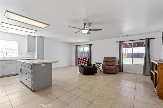 kitchen with light tile patterned floors, gray cabinets, ceiling fan, a center island, and sink