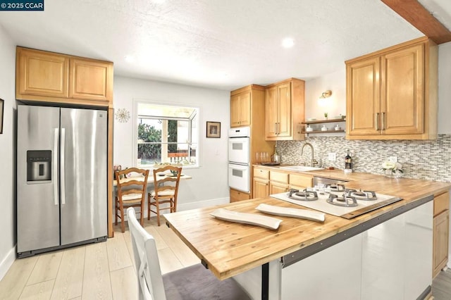 kitchen with butcher block countertops, backsplash, white appliances, light wood-type flooring, and sink