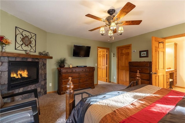 bedroom with ceiling fan, carpet, connected bathroom, and a stone fireplace