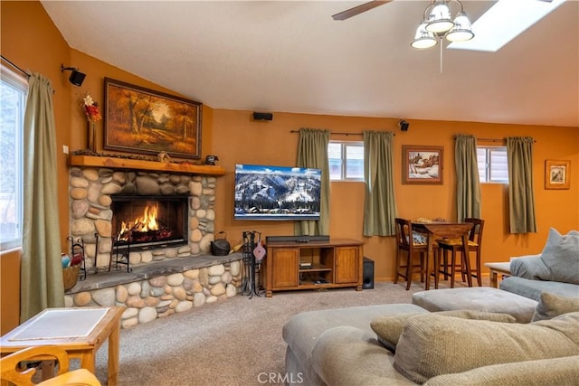 carpeted living room with ceiling fan, a stone fireplace, and vaulted ceiling