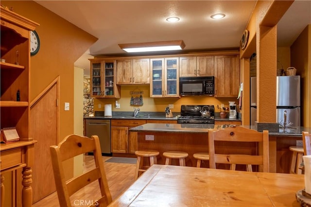 kitchen featuring light wood-type flooring, appliances with stainless steel finishes, a kitchen bar, and sink