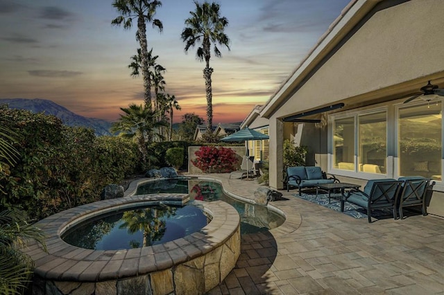 pool at dusk with an outdoor hangout area, a mountain view, an in ground hot tub, and a patio