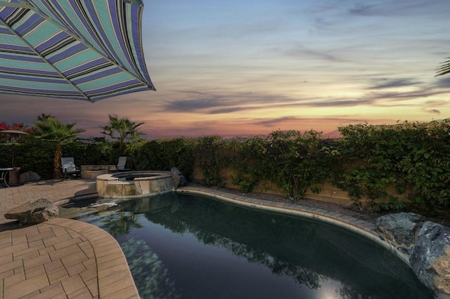 pool at dusk featuring a patio and an in ground hot tub