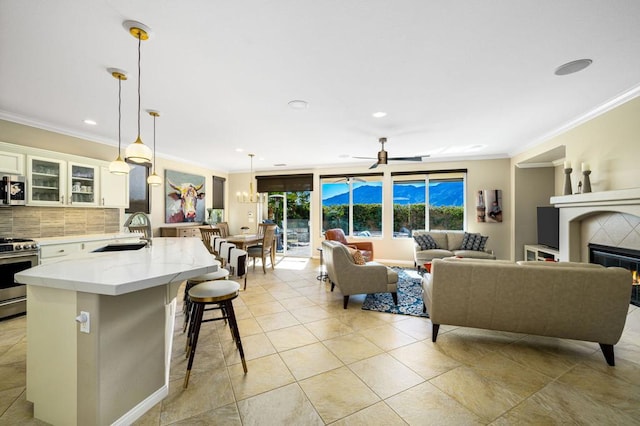 living room with ceiling fan, sink, crown molding, and a tiled fireplace