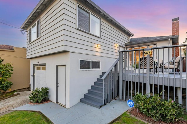 back house at dusk with a deck and a garage