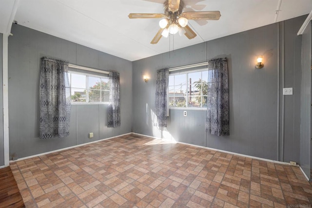 unfurnished room featuring ceiling fan, wood walls, and a healthy amount of sunlight