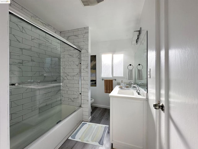 full bathroom with bath / shower combo with glass door, toilet, vanity, and hardwood / wood-style floors