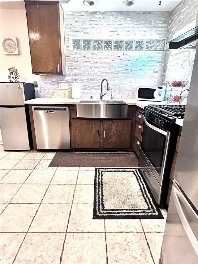 kitchen featuring decorative backsplash, light tile patterned flooring, sink, dark brown cabinetry, and stainless steel appliances