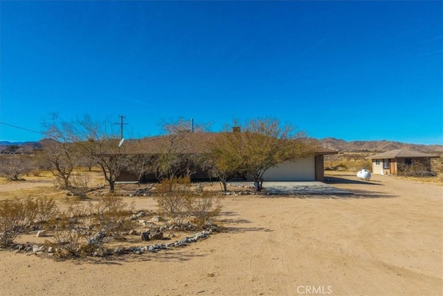 exterior space featuring an attached garage, dirt driveway, and a mountain view