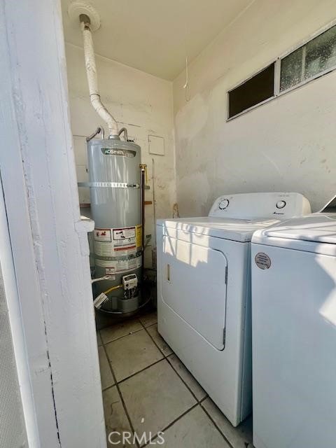 clothes washing area with light tile patterned floors, independent washer and dryer, and strapped water heater