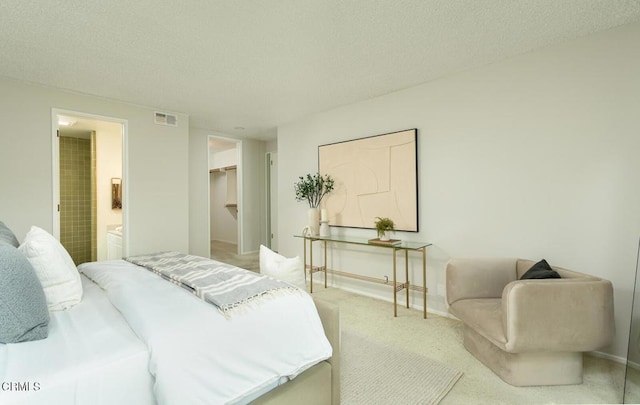 carpeted bedroom with a spacious closet, a textured ceiling, ensuite bathroom, and a closet