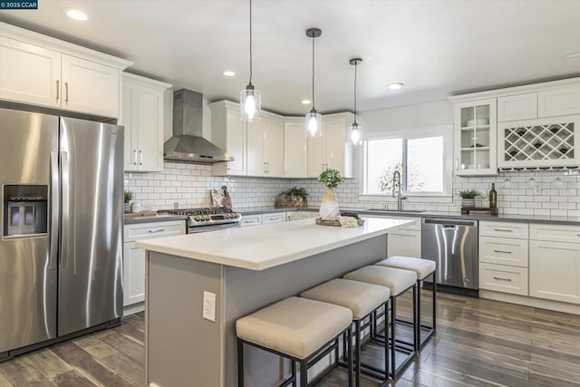 kitchen with decorative light fixtures, white cabinets, stainless steel appliances, and wall chimney exhaust hood