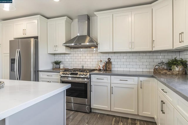 kitchen with appliances with stainless steel finishes, dark wood-type flooring, white cabinetry, wall chimney range hood, and backsplash