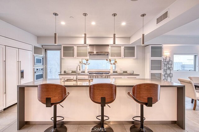 2618 Cove St, Corona Del Mar, CA 92625 - kitchen featuring stainless steel appliances, a sink, a breakfast bar, white cabinetry, and wall chimney exhaust hood