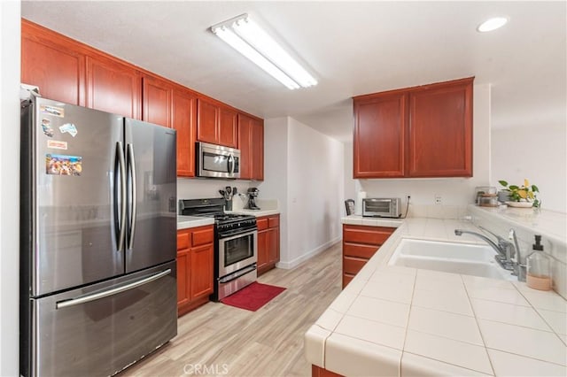 kitchen featuring appliances with stainless steel finishes, sink, tile countertops, and light hardwood / wood-style floors