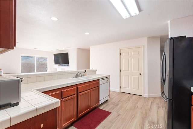 kitchen featuring tile counters, sink, light wood-type flooring, white dishwasher, and fridge