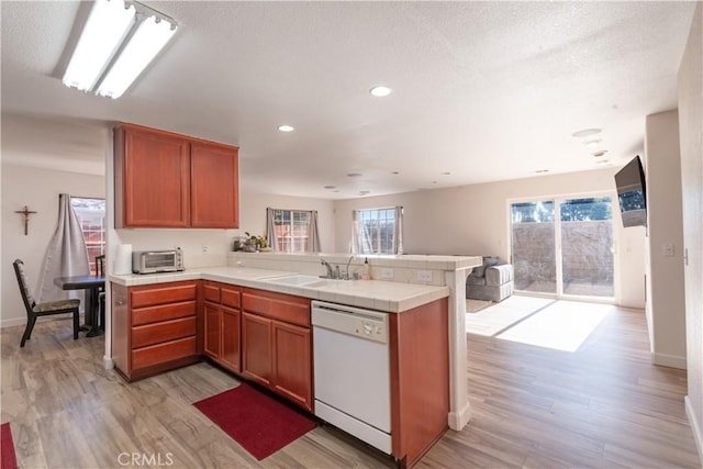 kitchen with light wood-type flooring, dishwasher, kitchen peninsula, and sink