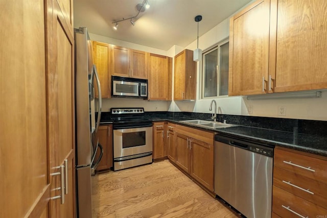 kitchen with dark stone countertops, pendant lighting, sink, light wood-type flooring, and stainless steel appliances