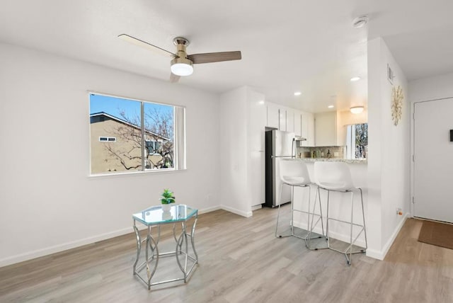 kitchen with kitchen peninsula, ceiling fan, tasteful backsplash, stainless steel refrigerator, and white cabinets