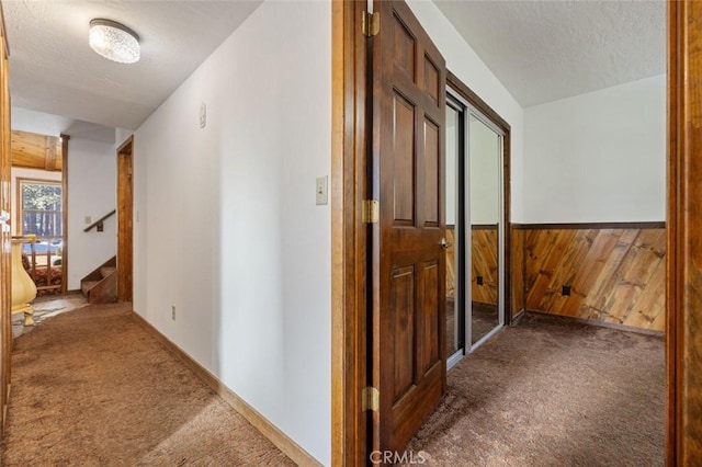 hall with a textured ceiling, wood walls, and carpet flooring