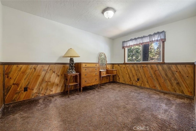 carpeted spare room with a textured ceiling and wood walls