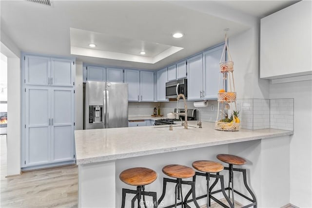 kitchen with a breakfast bar, stainless steel appliances, kitchen peninsula, and a tray ceiling