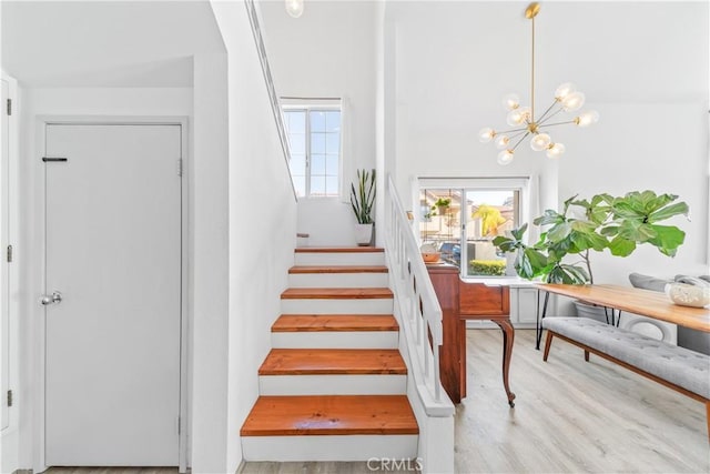 stairway featuring an inviting chandelier, a wealth of natural light, and wood-type flooring