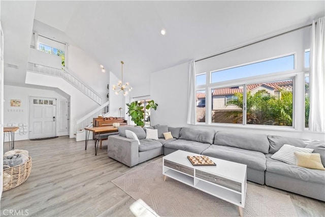 living room with light wood-type flooring, a towering ceiling, and an inviting chandelier