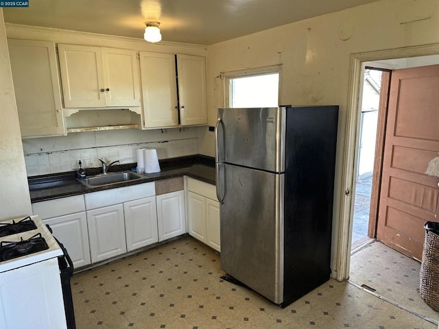 kitchen with stainless steel refrigerator, white cabinetry, sink, backsplash, and white gas stove