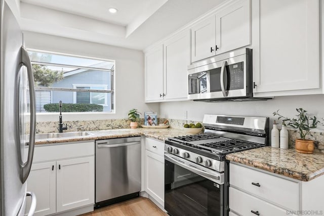 kitchen with light stone countertops, appliances with stainless steel finishes, white cabinets, and sink