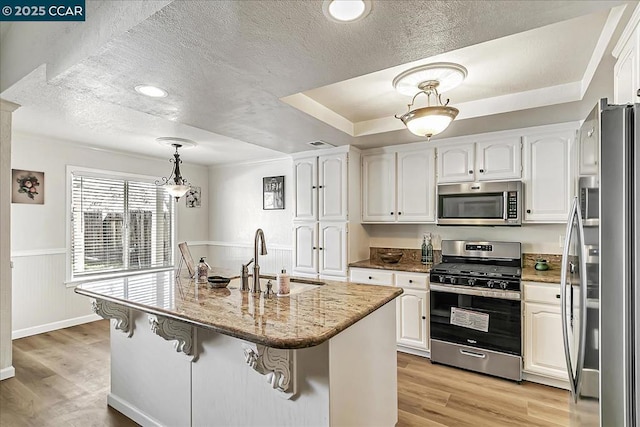 kitchen featuring a center island with sink, appliances with stainless steel finishes, decorative light fixtures, white cabinets, and sink