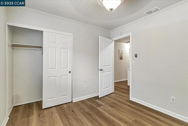 unfurnished bedroom with a closet, crown molding, and hardwood / wood-style floors