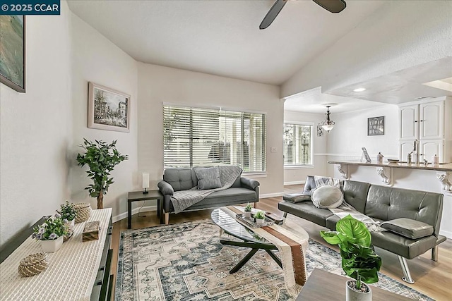 living room with ceiling fan, sink, lofted ceiling, and light wood-type flooring