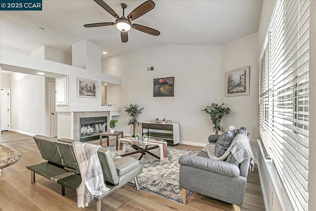 living room featuring ceiling fan, vaulted ceiling, a tile fireplace, and light wood-type flooring