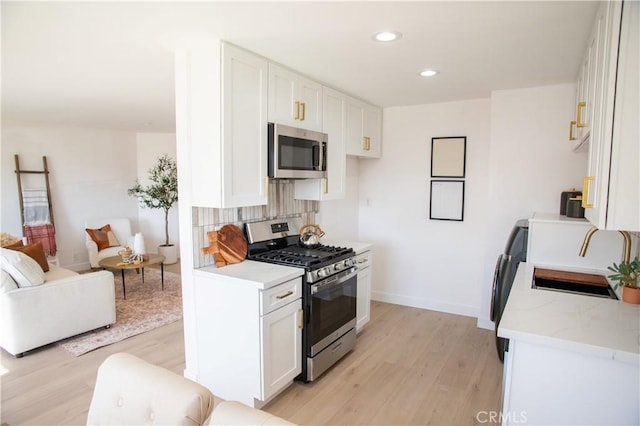 kitchen featuring white cabinetry, stainless steel appliances, decorative backsplash, light wood-type flooring, and light stone countertops