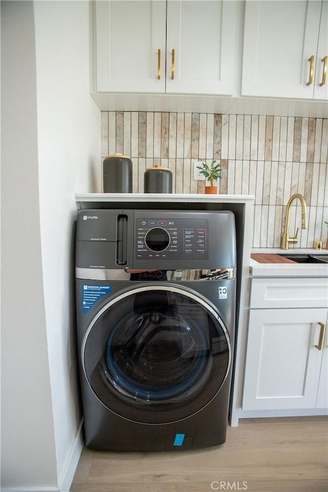 laundry area with light hardwood / wood-style floors, cabinets, washer / dryer, and sink